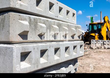 Blocchi di cemento grigio conservati in un cantiere con un escavatore giallo sullo sfondo. Foto Stock