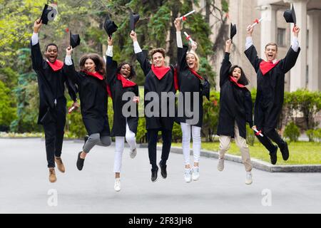 Felici studenti che festeggiano la laurea dall'università, saltando in su Foto Stock