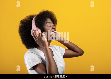 Gioiosa donna nera in cuffia wireless con cui ascoltare musica occhi chiusi  su sfondo giallo dello studio Foto stock - Alamy