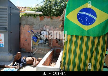 salvador, bahia, brasile - 21 gennaio 2021: L'uomo dorme sul pavimento accanto ad una bandiera brasiliana in una baracca nel quartiere di Itapua, nella città di Salv Foto Stock