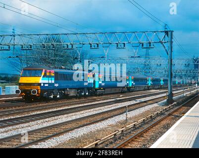 Una locomotiva elettrica di classe 90 numero 90003 che aziona un treno di giacenze Mk3 corrispondenti nella nuova livrea colorata del franchising "One" passato Pudding Mill Lane il 1 aprile 2004. Questo treno è stato il lancio speciale per il nuovo franchising "One" che in seguito è diventato National Express East Anglia (NXEA). Foto Stock