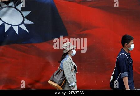 Taipei, Taiwan. 11 Apr 2021. I taiwanesi che indossano una maschera facciale camminano oltre un'enorme bandiera con una bandiera nazionale di Taiwan in mezzo alle tensioni aumentate con la Cina. Con Pechino che invia più jet fighter che navigano intorno all'isola, il ministro degli Esteri di Taiwan Joseph Wu ha detto che Taiwan si difenderà al "ventoso ultimo giorno", mentre sta promuovendo relazioni con gli Stati Uniti in materia di militare, economia, tecnologia e servizi medici. Credit: Daniel Ceng Shou-Yi/ZUMA Wire/Alamy Live News Foto Stock