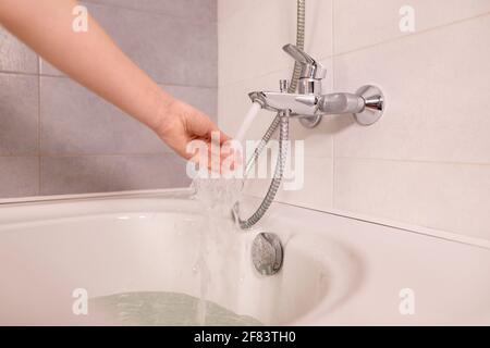 Donna prendere bagno a casa controllando la temperatura toccando acqua corrente con mano. Dita sotto acqua calda da un rubinetto di un lavello o vasca da bagno in casa b Foto Stock