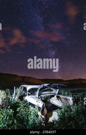 auto abbandonata nel mezzo di un campo di notte con il senso lattiginoso dietro Foto Stock