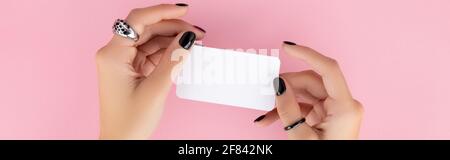 Womans manicured mano che tiene cartolina su pinkbackground Foto Stock