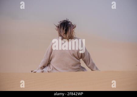 Donna seduta sulla duna di sabbia in un umore contemplativo Foto Stock