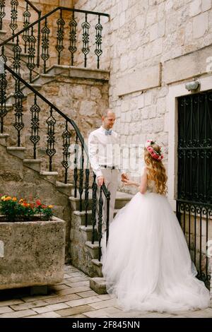 La sposa e lo sposo si trovano su una stretta scala con Una bella ringhiera in ferro battuto nella città vecchia di Cattaro Foto Stock