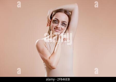 Ritratto di giovane donna che posa con applicato macchie di bellezza nere sotto gli occhi su sfondo beige. Foto Stock