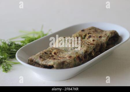 Pane piatto indiano fatto di farina integrale con semi di lino macinato e foglie di coriandolo fresco. Localmente noto come coriandolo paratha. Ripresa sulla parte posteriore bianca Foto Stock