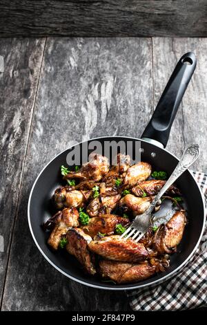 Ali di pollo arrosto in padella su tavolo di legno Foto Stock