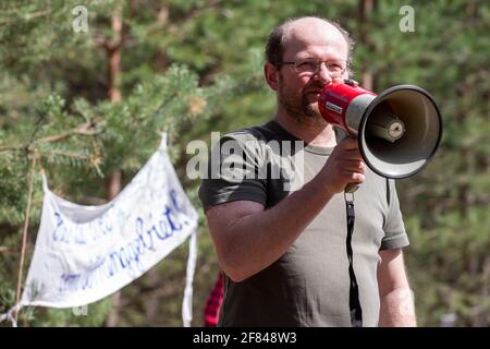 Schleife, Germania. 11 Apr 2021. René Schuster del gruppo ambientale della Green League Cottbus parla ai circa 60 partecipanti del rally con un megafono. L'azione di protesta 'non vendibile' della rete ambientale Green League a Schleife, nei pressi della buca aperta Nochten, nel distretto di Görlitz, è diretta contro il minacciato dragaggio di LEAG (Lausitz Energie Bergbau AG). Credit: Daniel Schäfer/dpa-Zentralbild/dpa/Alamy Live News Foto Stock