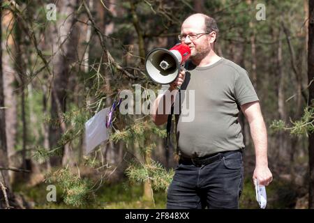Schleife, Germania. 11 Apr 2021. René Schuster del gruppo ambientale della Green League Cottbus parla ai circa 60 partecipanti del rally con un megafono. L'azione di protesta 'non vendibile' della rete ambientale Green League a Schleife, nei pressi della buca aperta Nochten, nel distretto di Görlitz, è diretta contro il minacciato dragaggio di LEAG (Lausitz Energie Bergbau AG). Credit: Daniel Schäfer/dpa-Zentralbild/dpa/Alamy Live News Foto Stock
