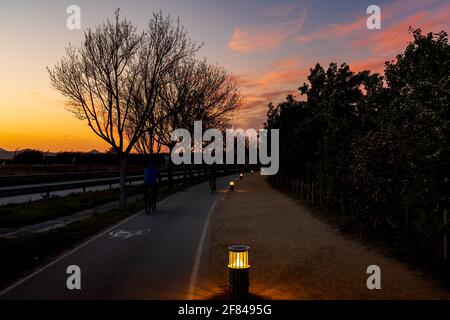 Strada rurale nel delta di Llobregat, a Barcellona. Possiamo vedere un sentiero di sabbia, una pista ciclabile e una strada dall'altro lato. Al centro ci sono le illumine Foto Stock