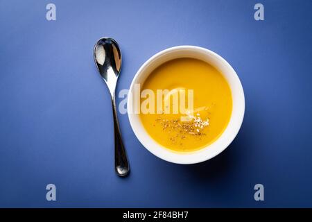 Zuppa vegetariana di crema vegetale in una ciotola bianca con crostini su sfondo blu, vista dall'alto Foto Stock