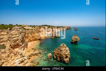 Vista su scogliere di rocce arenaria scoscese, formazioni rocciose nel mare turchese, spiaggia sabbiosa sulla scogliera, Praia da Marinha, Algarve, Lagos, Portogallo Foto Stock