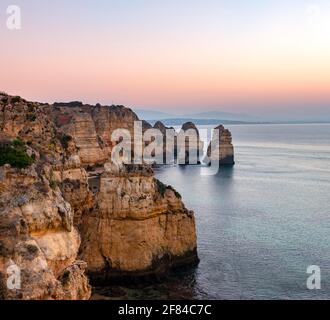 Aspra costa rocciosa con scogliere di arenaria, formazioni rocciose nel mare, Ponta da Piedade, Dawn, Algarve, Lagos, Portogallo Foto Stock