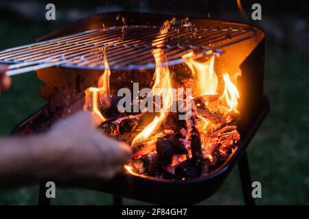 Mescolando le braci del barbecue. Preparazione del fuoco per un barbecue all'aperto di notte. Foto Stock