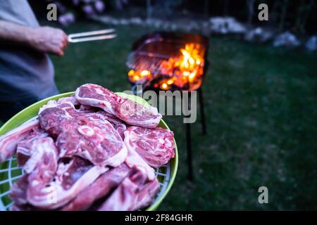 Carne cruda da cuocere al barbecue con il fuoco che si fa brillare. Preparazione di carne alla griglia in giardino di notte. Foto Stock