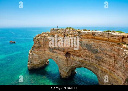 Giovane donna in piedi su una roccia sulla scogliera, vista di rupe di rocce arenaria scoscesa, archi di roccia in mare turchese, Praia da Marinha, Algarve, Lagos Foto Stock