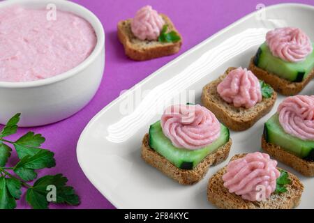 Un piatto bianco con crostini taramosalata e una ciotola bianca con tarama sullo sfondo viola primo piano Foto Stock