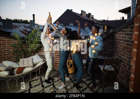 Ritratto completo di amici gioiosi che si rilassano con bevande alcoliche e musica preferita durante la festa. Concetto di relax, multietnicità e spensieratezza. Foto Stock