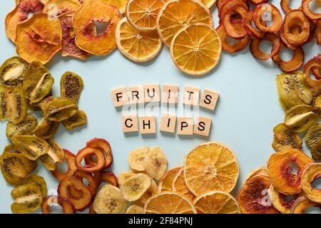 Prugne secche a fette, kiwi, patatine di frutta di pesca su sfondo blu e testo - patatine di frutta. Snack vegan senza zucchero cibo. Vista dall'alto. Foto Stock