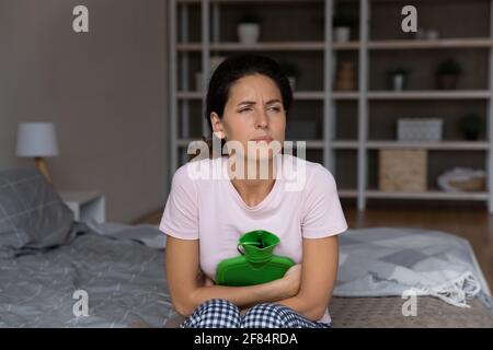 Giovane donna con dismenorrea che scalda la pancia con bottiglia d'acqua calda Foto Stock