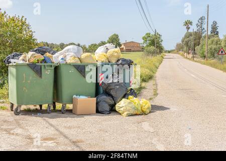 Campos, Spagna; aprile 10 2021: Tre contenitori per rifiuti pieni di sacchi per rifiuti all'interno e con più sacchi per rifiuti a terra su una strada rurale sulla isl Foto Stock