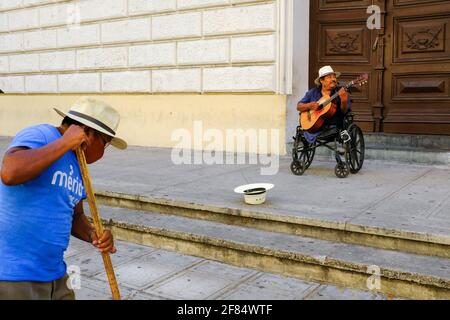 Operaio della città che pulisce la strada mentre un musicista di strada canta - durante la pandemia di Covid-19 a Merida messico Foto Stock