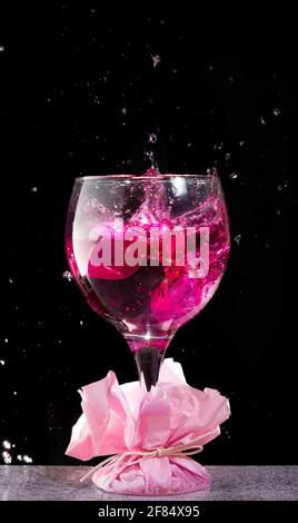 bevanda alcolica rosa che cade in calice di vetro su sfondo nero Foto Stock
