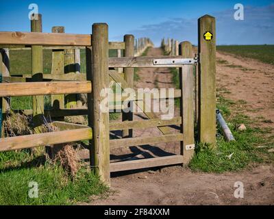 Una porta di bacia in legno dà accesso ad un percorso lungo il bordo di un campo. Preso in un'area rurale nel nord-ovest dell'Inghilterra nel Regno Unito in una giornata soleggiata in Foto Stock