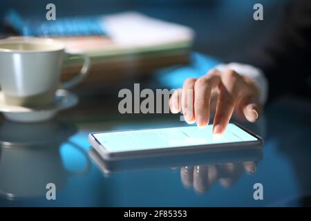 Primo piano di una mano d'affari che firma on-line su Smart telefono di notte in ufficio Foto Stock