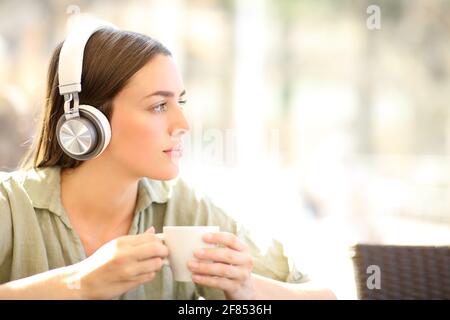 Donna che indossa le cuffie wireless che rilassa l'ascolto della musica tazza in una caffetteria Foto Stock