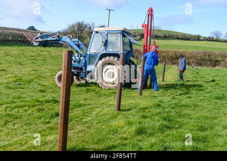 Due agricoltori usano un pilota idraulico per installare pali di recinzione in un campo, Irlanda del Nord. Foto Stock