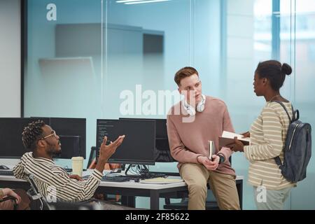 Diversi gruppi di giovani che discutono di progetto mentre lavorano insieme in ufficio o in laboratorio INFORMATICO scolastico con computer, spazio di copia Foto Stock