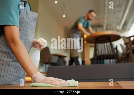 Primo piano di una cameriera femminile irriconoscibile tavolo di pulizia in caffetteria con caldi accenti di legno, spazio copia Foto Stock