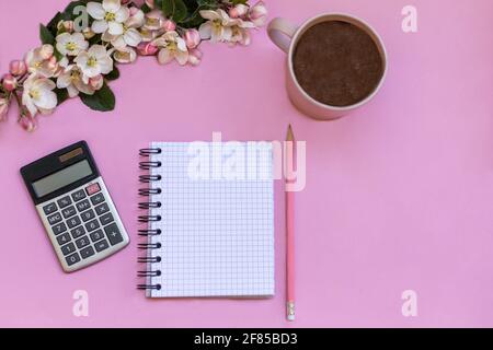 Un notebook per le note si trova su uno sfondo rosa, accanto a penna, calcolatrice, caffè e fiori. Pianificazione del budget personale Foto Stock