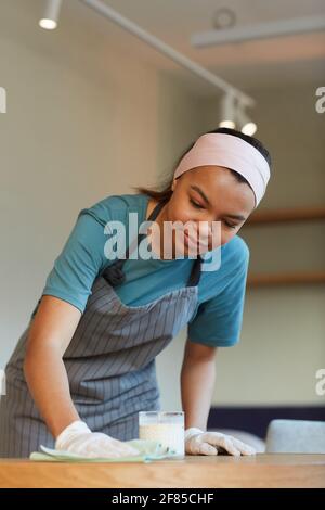 Ritratto verticale del tavolo per la pulizia delle cameriere da corsa mista in un bar o una caffetteria mentre si preparano per l'apertura di mattina Foto Stock