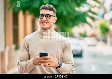 Giovane uomo ispanico che indossa occhiali utilizzando smartphone in città. Foto Stock