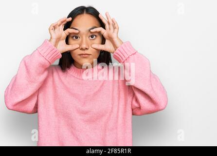 Giovane donna asiatica che indossa un maglione invernale casual cercando di aprire gli occhi con le dita, sonnolenta e stanca per stanchezza mattutina Foto Stock