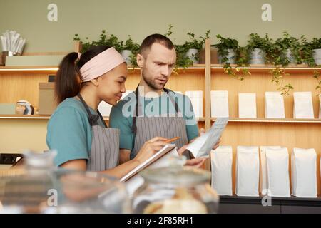 Vita in su ritratto di due camerieri giovani che indossano grembiuli mentre fanno l'inventario nel caffè o nella caffetteria, spazio di copia Foto Stock