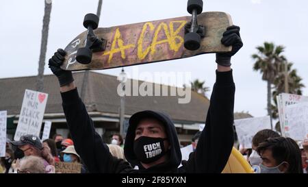 Huntington Beach, California, Stati Uniti. 11 Apr 2021. Un uomo tiene uno skateboard con un messaggio anti-polizia verso gli ufficiali di polizia durante una controrprotesta contro un raduno 'White Lives Matter' sul molo di Huntington Beach. Credit: Young G. Kim/Alamy Live News Foto Stock