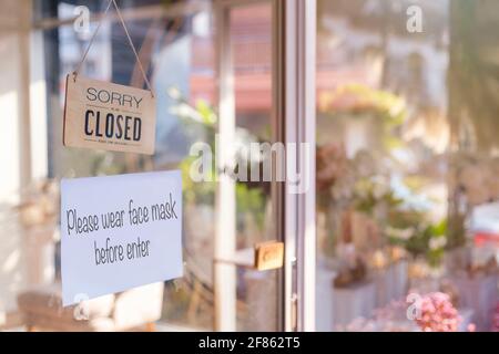 Siamo spiacenti siamo chiusi cartello legno e si prega di indossare la maschera per entrare in carta su porta di vetro protezione per pandemia di coronavirus. Chiudi negozio, ristorante Foto Stock