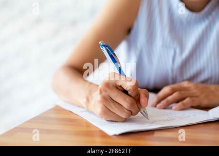 Primo piano mano di donne di affari usa carta di documento di scrittura della penna. Mano femminile primo piano con una penna blu su un foglio bianco. Donna scrive informatio Foto Stock
