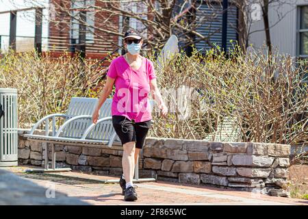 Frederick, MD, USA 04-07-2021: Una donna caucasica di mezza età che indossa pantaloncini, t-shirt e sneakers è a piedi per uno stile di vita sano nel parco di sunn Foto Stock