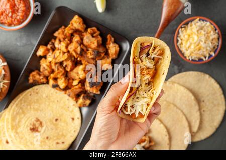 Immagine closeup di un piatto messicano di taco con tortillas di mais, pezzi di pollo precotti, prepreparati, cavolo, formaggio grattugiato, salsa di salsa e crema Foto Stock