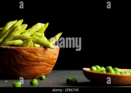 Closeup immagine isolata di una ciotola di legno riempita con croccante raccolto verde snacks piselli, un'alternativa più sana e nutriente alle patatine. Vista laterale Foto Stock