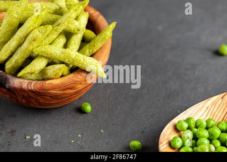 Closeup immagine isolata di una ciotola di legno riempita con croccante raccolto verde snacks piselli, un'alternativa più sana e nutriente alle patatine. Vie angolate Foto Stock