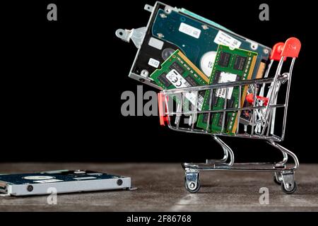 Un'immagine concettuale con un piccolo carrello della spesa pieno di componenti del computer, tra cui schede di memoria RAM e un disco rigido. Acquisto di tecnologia, consumatori e Foto Stock