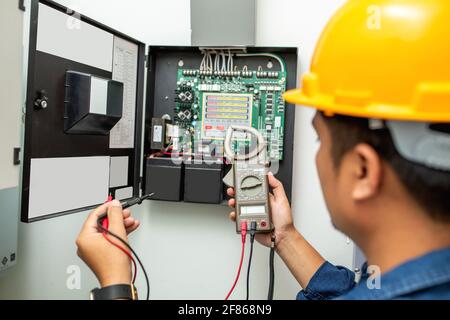 Gli elettricisti che lavorano utilizzano il multimetro a pinza digitale nelle mani di elettricisti, in primo piano sullo sfondo di fili elettrici e relè. Adeguamento del regime Foto Stock